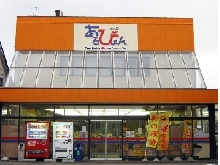 外壁がオレンジ色で店舗左前に自動販売機が2台並び、右側にのぼり旗が置かれている街の駅あるびょんの全体を写した写真