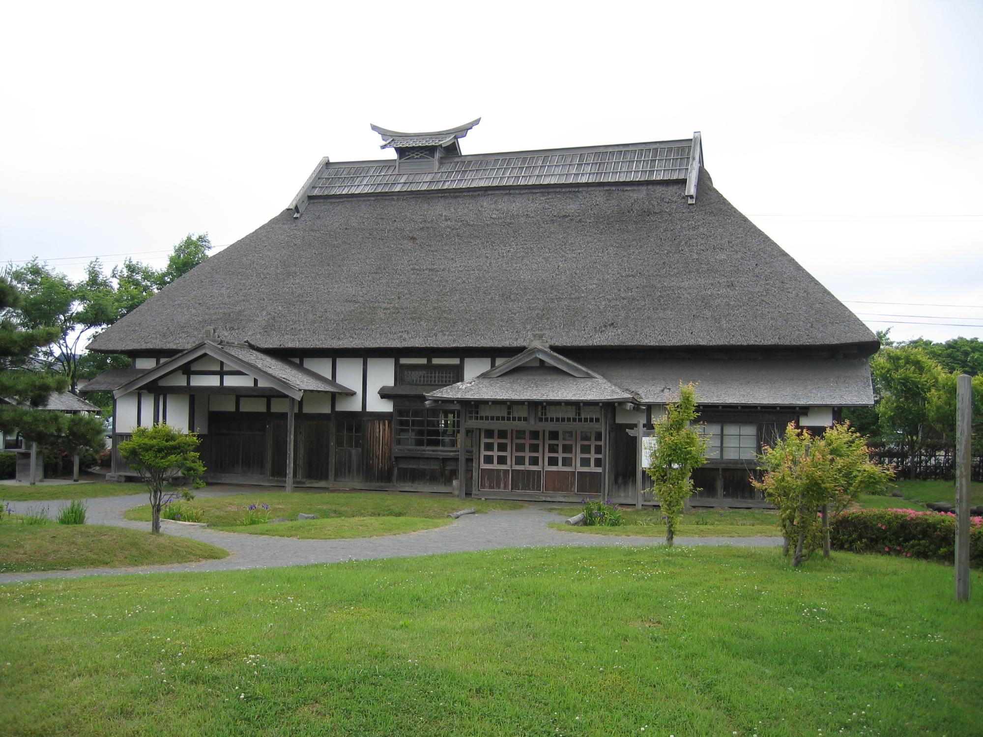 茅葺き民家で、周りに鮮やかな緑の芝生が植えられている旧尾野家住宅の外観全体を写した写真