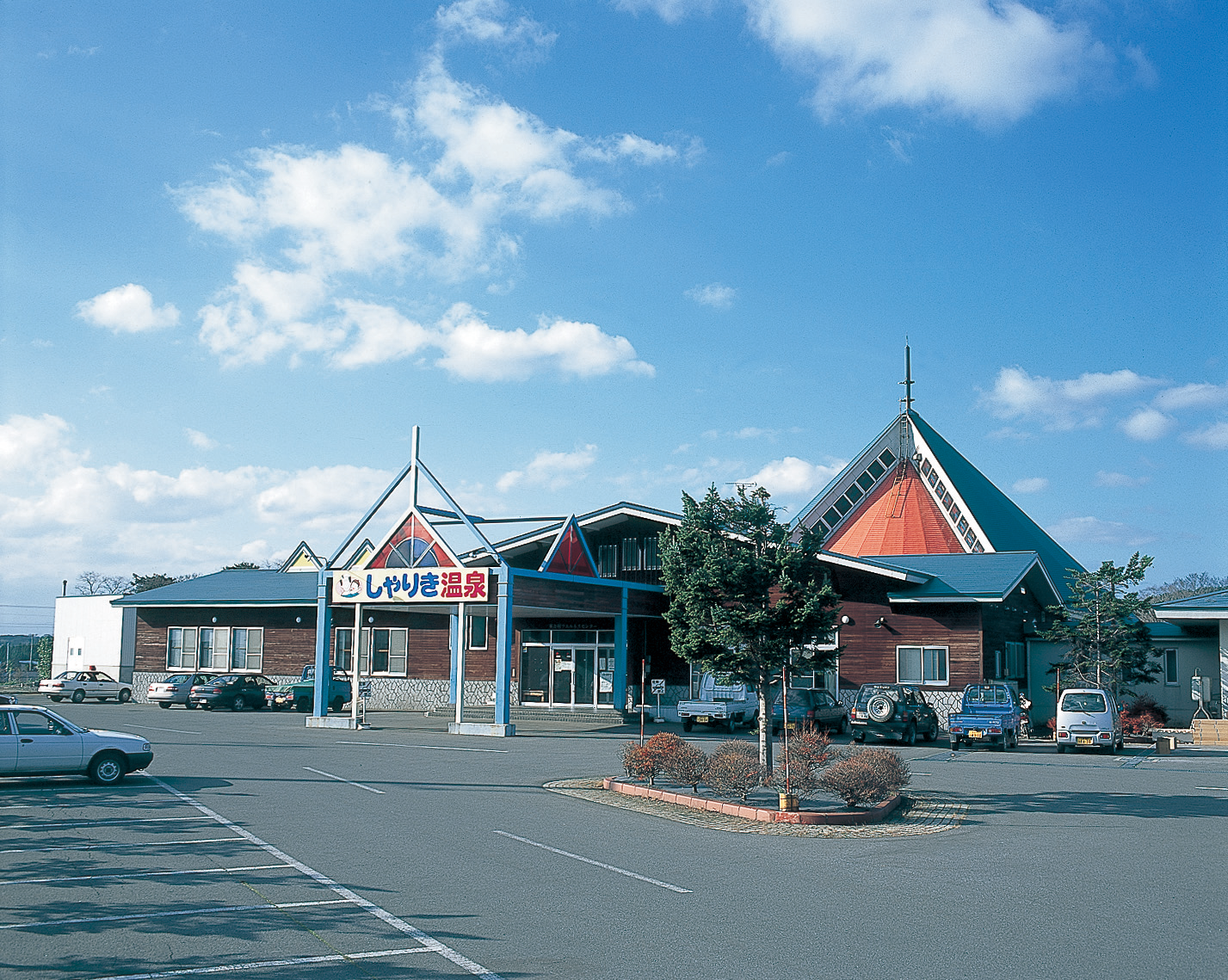温泉マークに「しゃりき温泉」と書かれた看板が設置され、特徴的な三角屋根が複数ある作りになっているウェルネスセンターしゃりき温泉の外観写真