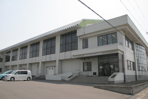 白色の外壁で2階は窓がたくさんあり、玄関入口には階段が設置され建物前には駐車スペースがある柏総合体育センター外観写真