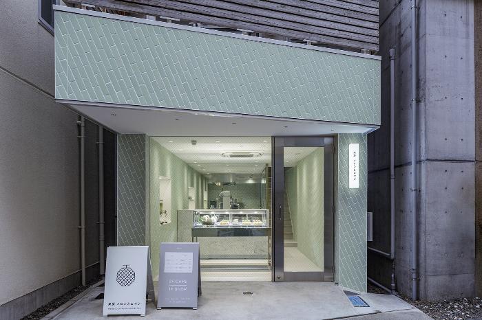正面に「果房 メロンとロマン」の看板が置かれており、コンクリートと薄いグリーンのタイルを基調とした店構えで、ガラス張りの正面側から店内を見た外観写真