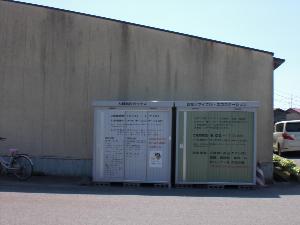 大きな建物の横に設置されている衣類回収ボックスと古紙リサイクルエコステーションのひき写真