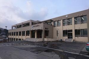 ベージュ色の外壁で2階建てになっており玄関入口前が駐車スペースになっている車力小学校の外観写真