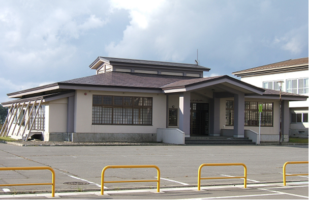 クリーム色の外壁、屋根が赤茶色系で格子の窓がある富萢地区コミュニティセンターの外観写真