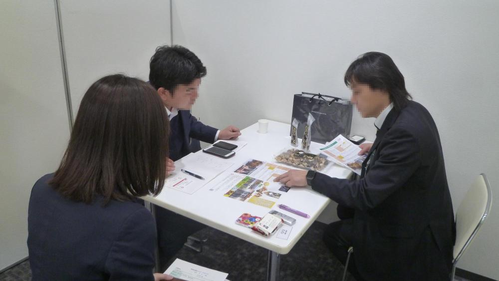 机を囲むように3人の方が座っており、机にはパンフレットが置かれ説明を受けている商談の様子の写真