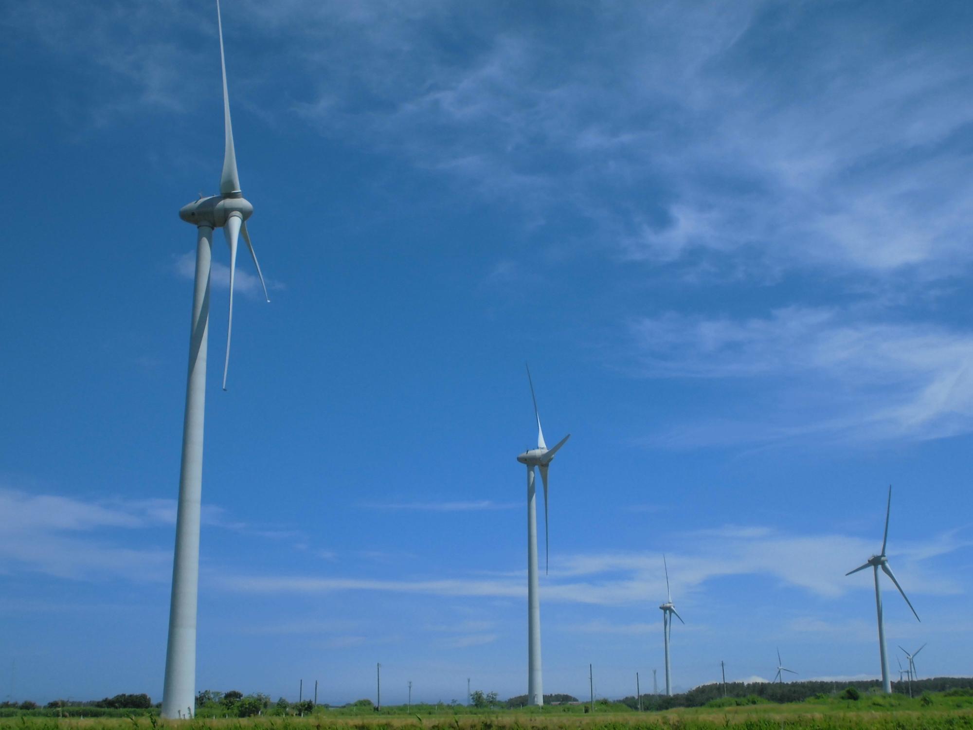 緑が広がる開けた場所に設置されているまほろば風力発電の風力タービンの写真