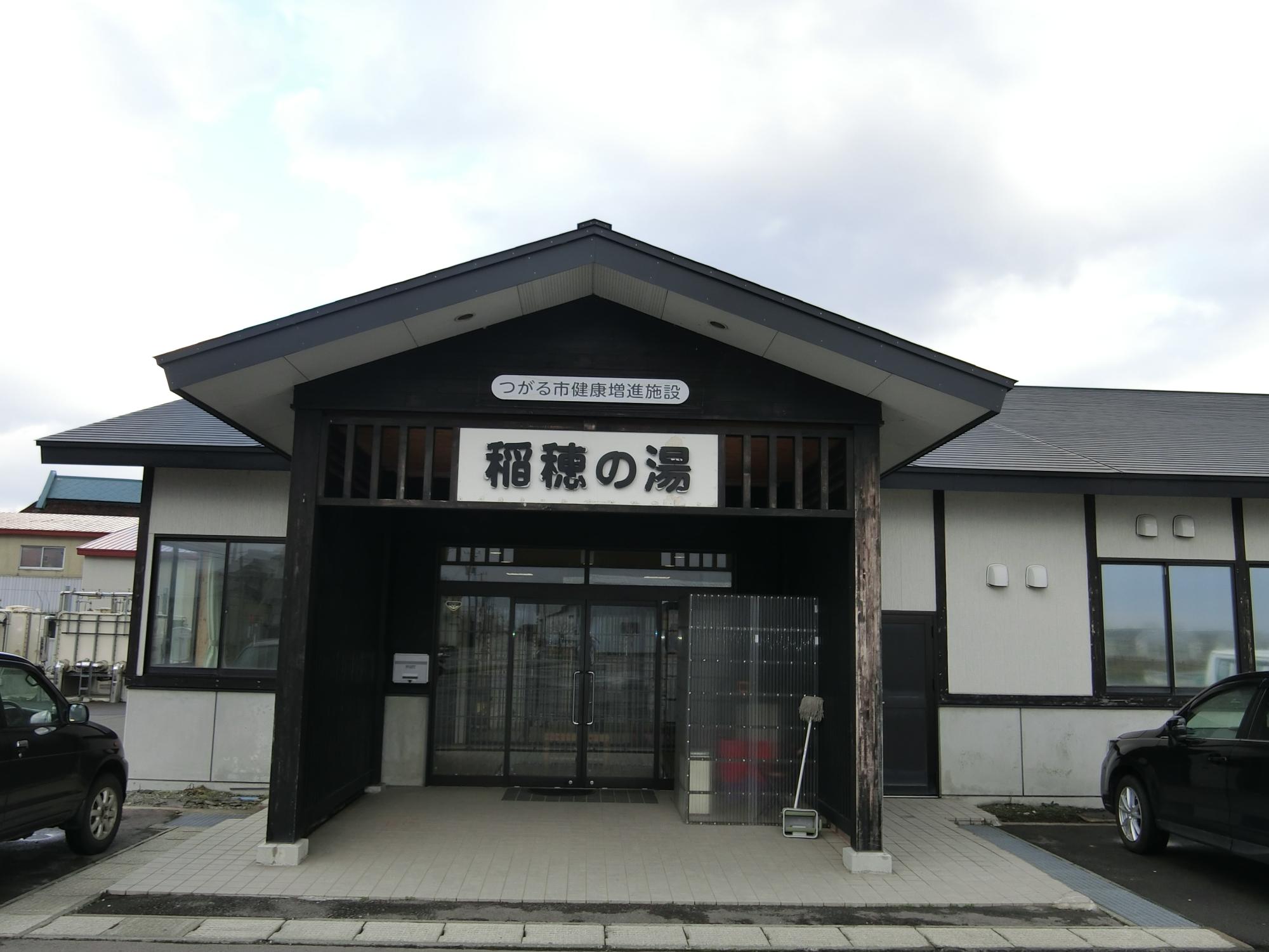 大きな三角屋根の入り口に「稲穂の湯」と書かれた看板が掲示されているつがる市健康増進施設 稲穂の湯を正面から写した写真