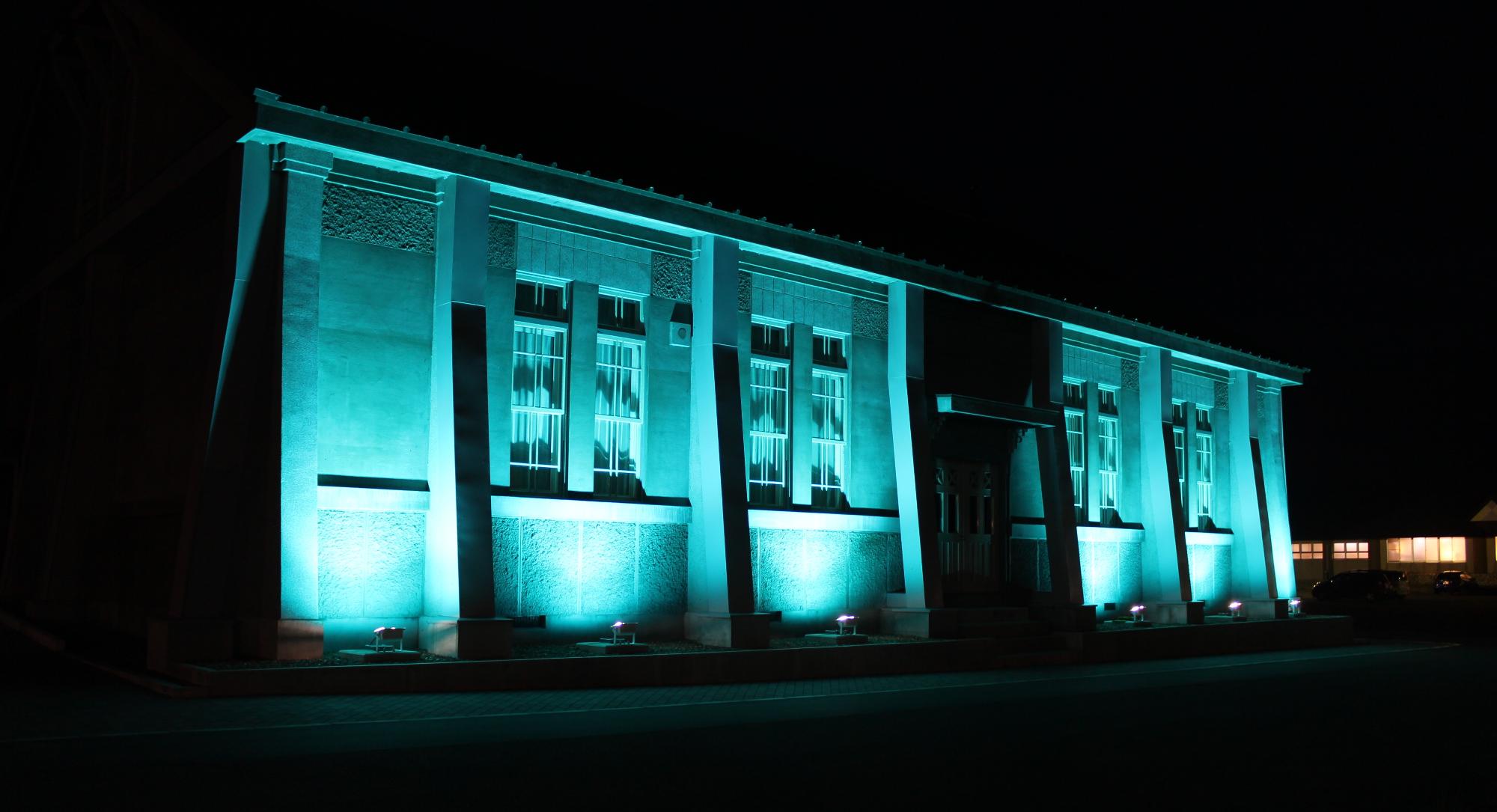 ブルーライトでライトアップされ幻想的に見える旧制木造中学校講堂の写真