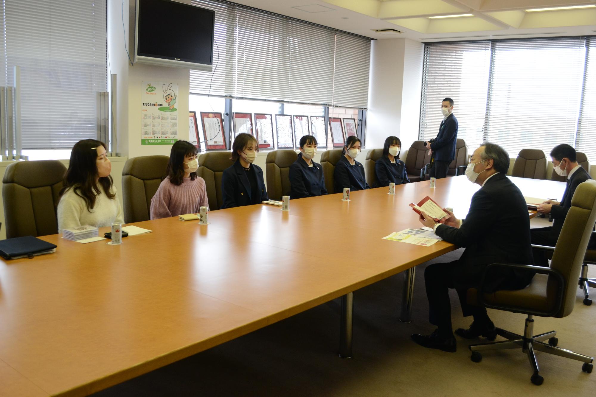 【新解釈つがる。辞典】編纂プロジェクトメンバー6名が市長を表敬訪問し横長の大きな机に市長と向かい合って座っている写真