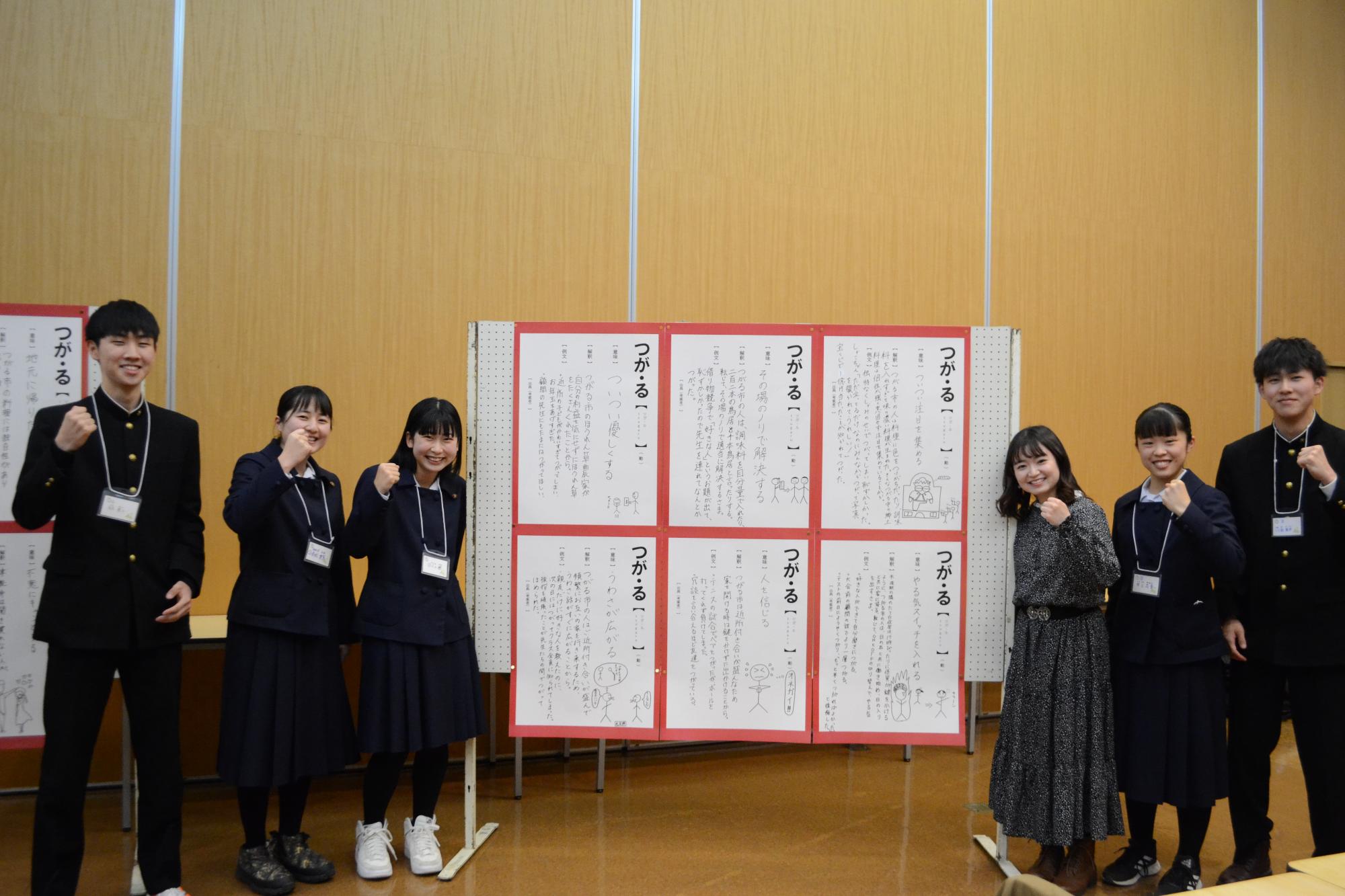 6枚のポスターが貼られたパネルを中心に左に3名、右に3名の参加者がガッツポーズして立っている写真
