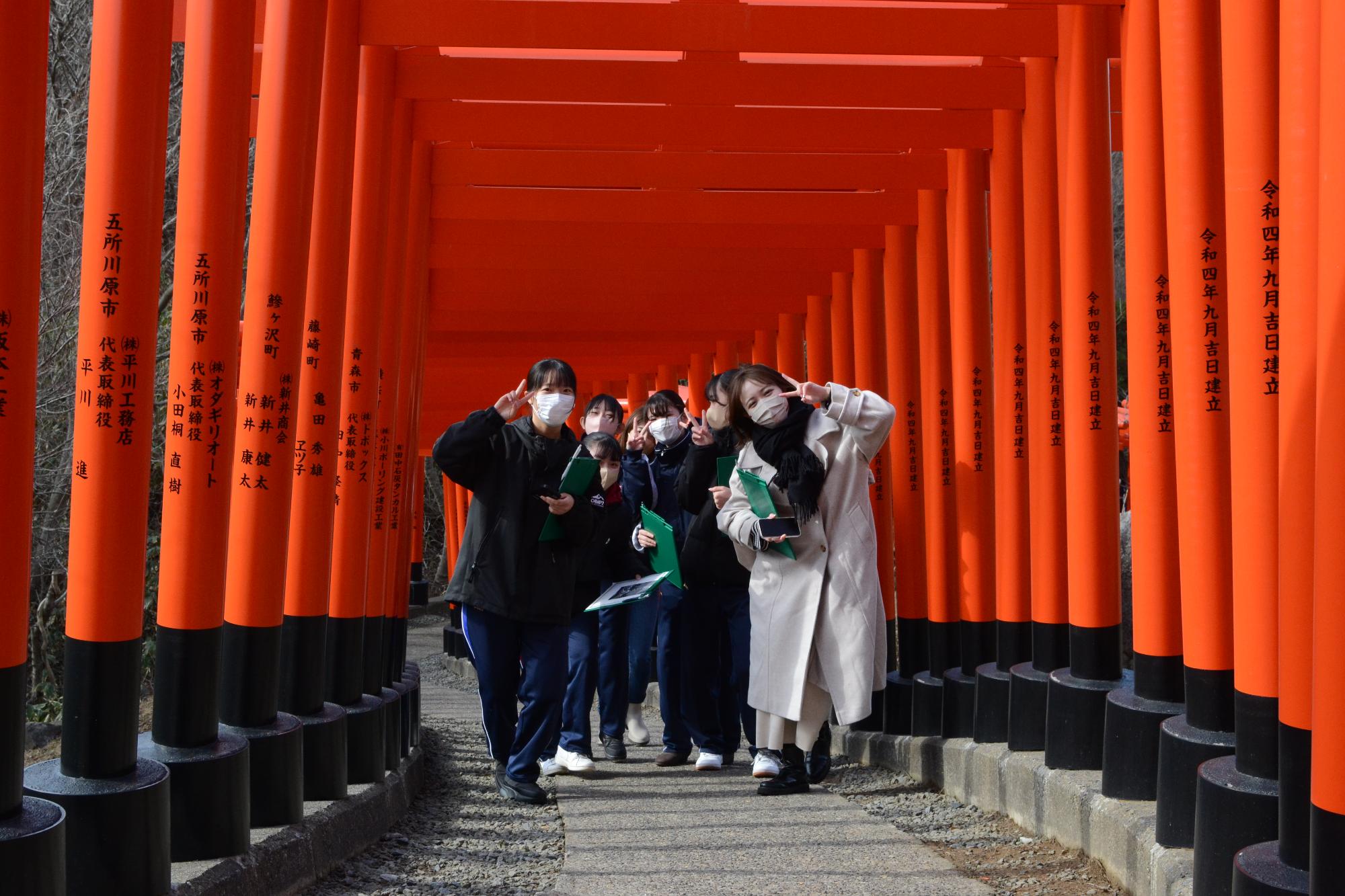 いくつもの赤い鳥居が奥へと続いている中でピースサインをして写真に写っている参加者たちの写真