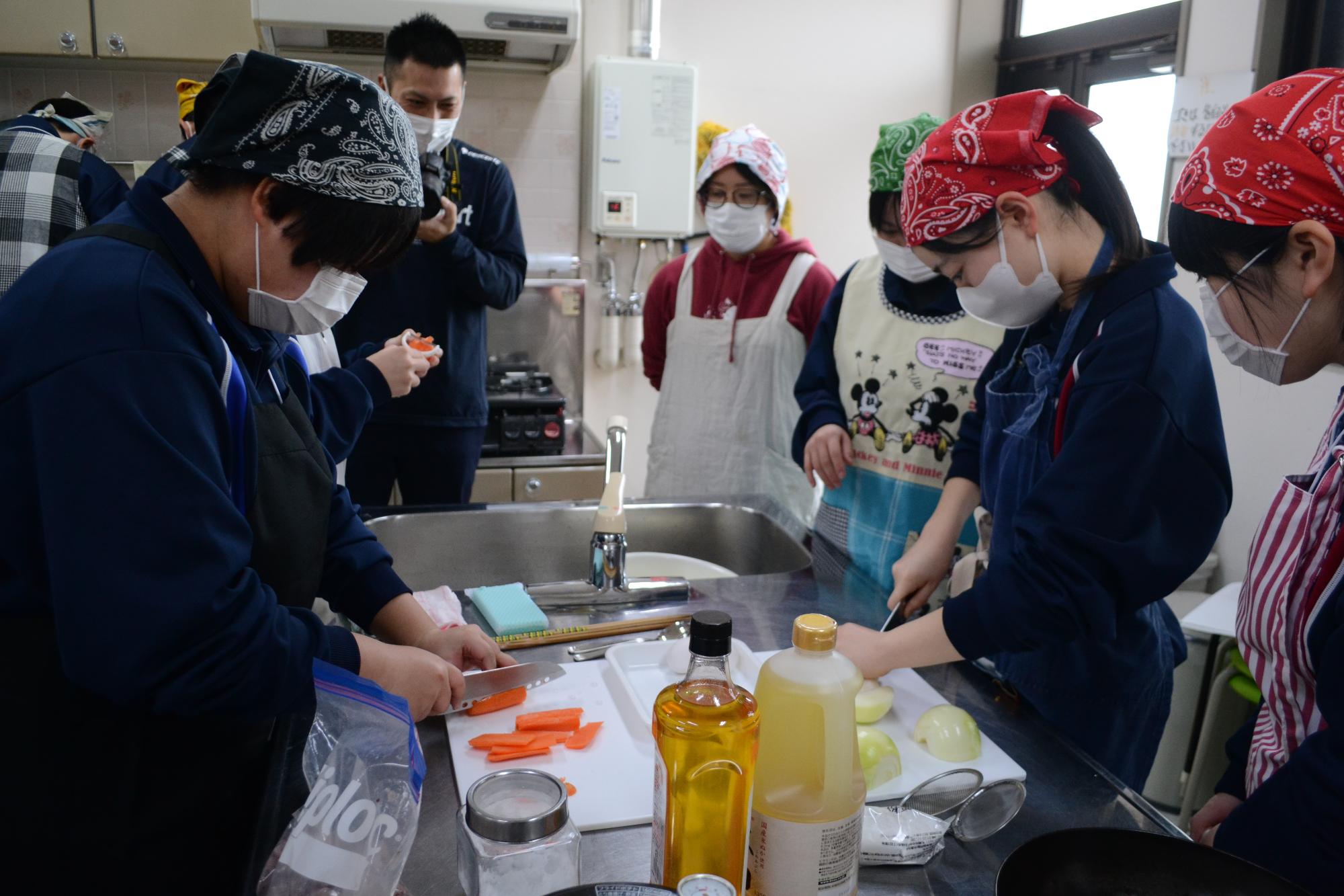 エプロンとバンダナを付けて野菜を切っている参加者たちの写真