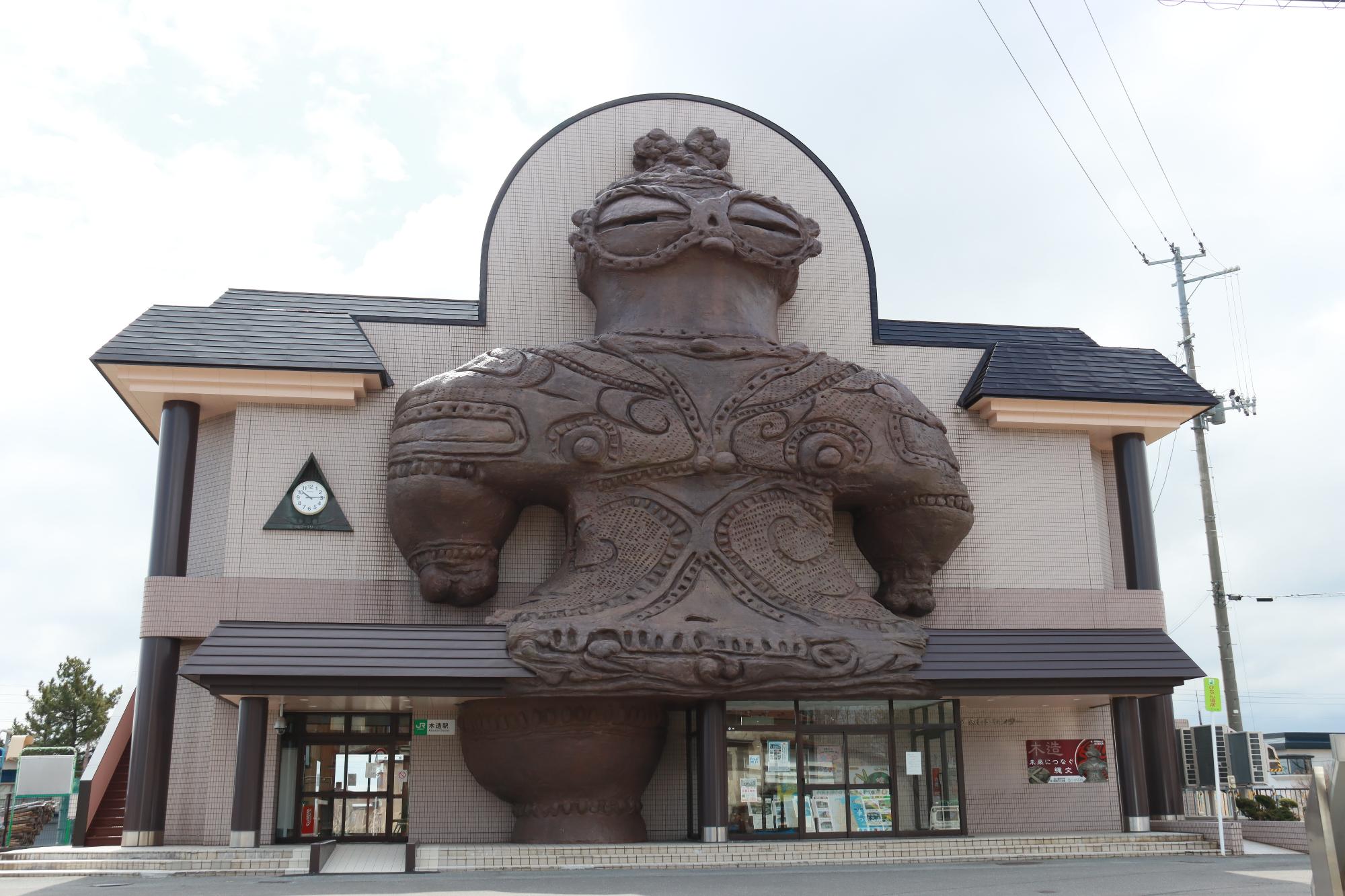 亀ヶ岡石器時代遺跡から出土した遮光器土偶（しゃこちゃん）の巨大モチーフを外壁に飾った迫力ある木造駅外観の写真