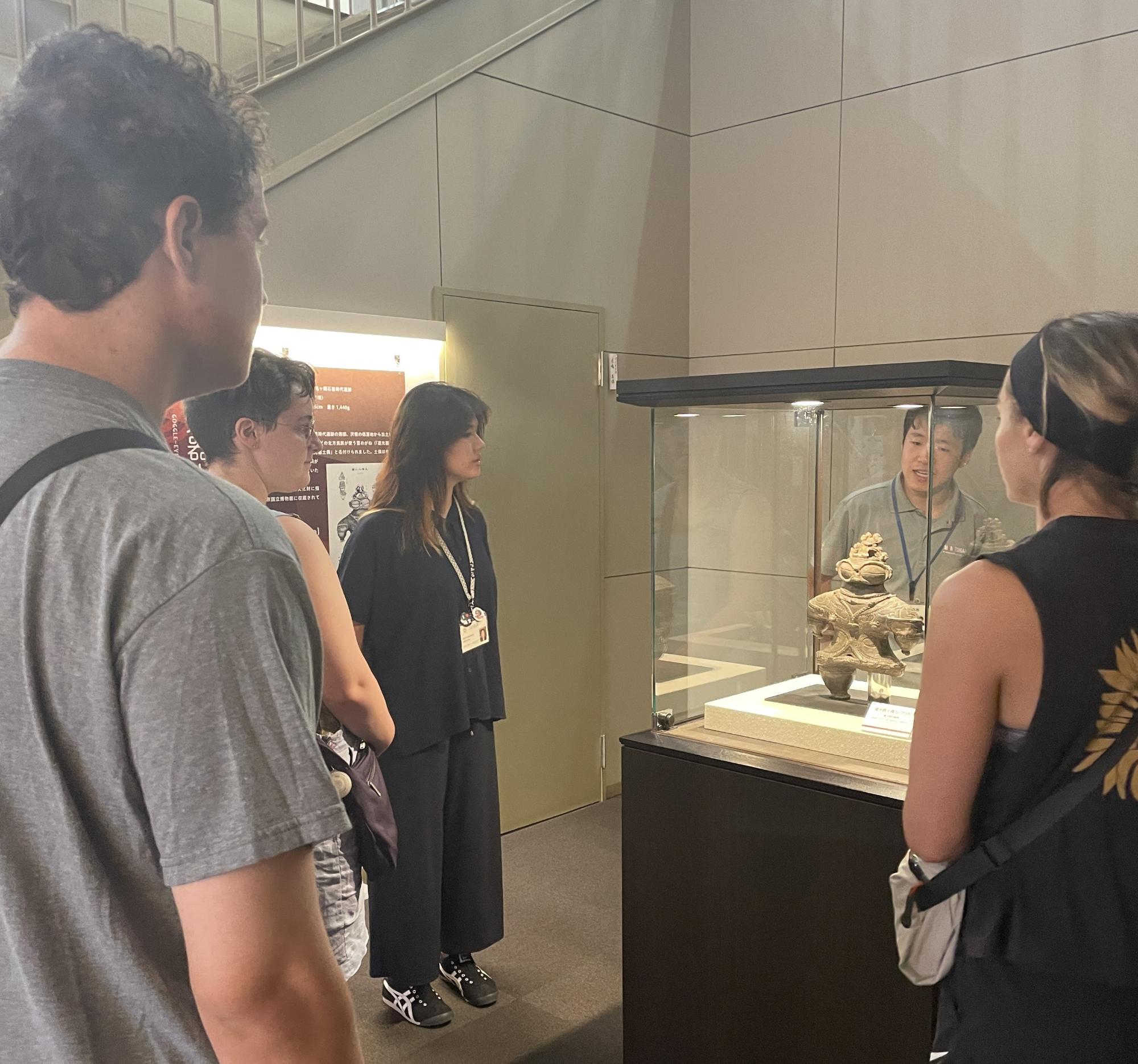 縄文住居展示資料館カルコ内にある縄文土器の展示品の前で関係者が訪問団に向けて説明をしているツアーの様子を撮影した写真
