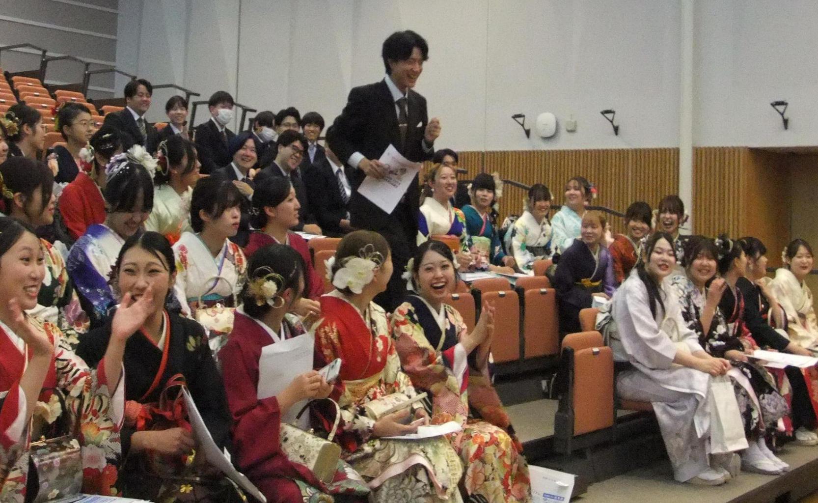 スーツを着た男性が抽選に当選し、座席から異動する様子と、それを見て盛り上がる参加者の写真