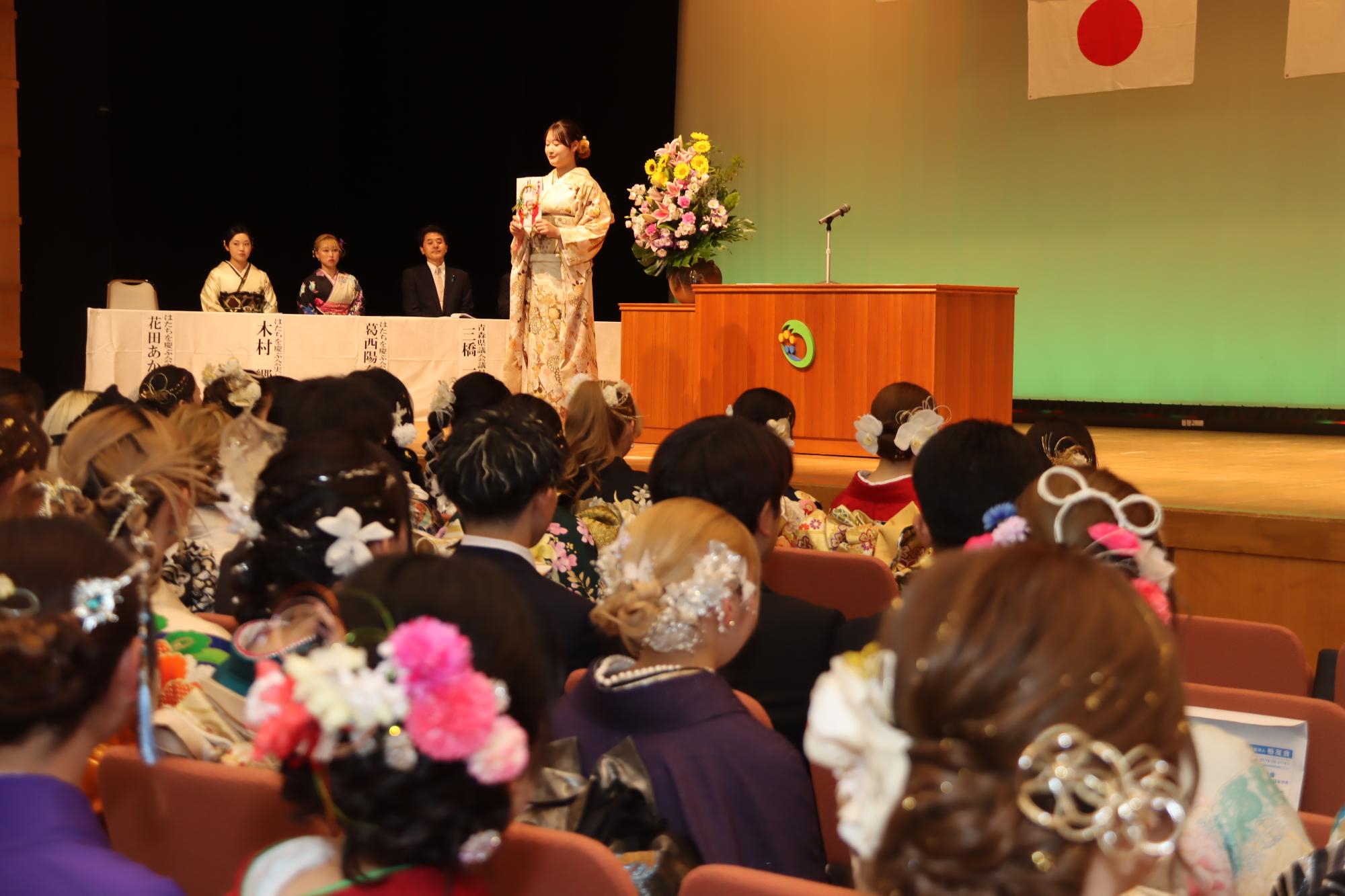 式典で記念品を受け取っている代表者を見ている参列者