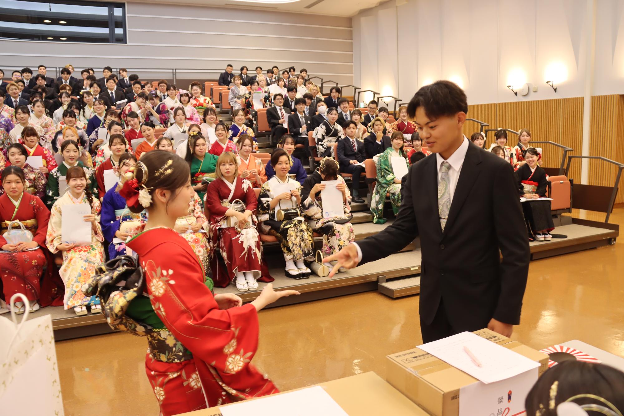 スーツを着た男性と振袖を着た女性が当選し、2つの景品を選ぶ順番を決めるためのじゃんけんをする様子